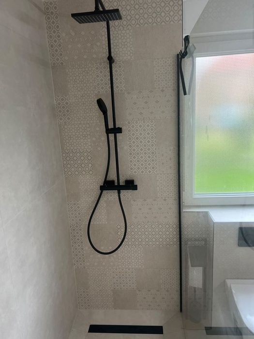 Badezimmer nach der Sanierung: begehbare Dusche mit gemusterten Fliesen und schwarzer Armatur